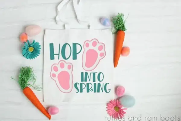 hop into spring svg placed on Easter tote bag on white wood background with craft flowers and carrots