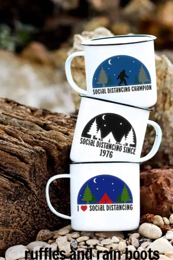 three camp mugs with social distancing svg designs on them in front of wood in the forest and a pebble beach