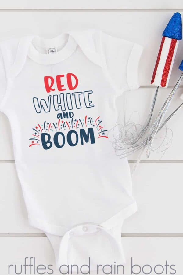 close up of white onesie on white wood background with red white and boom svg and fireworks