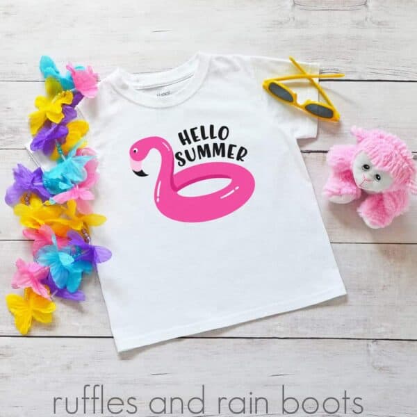 adorable hello summer svg flamingo pool float on a kids shirt laying on a table with summer toys