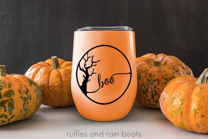 boo with spooky tree design in black on orange mug with pumpkin and wood background