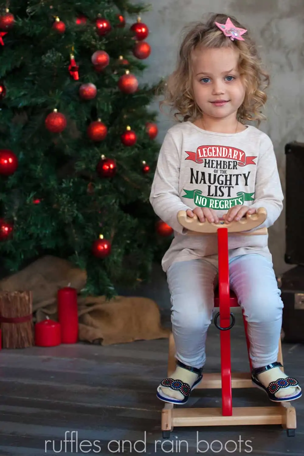vertical image of a little girl on a scooter in front of a Christmas tree wearing a sweatshirt with a naughty list svg in red green and black