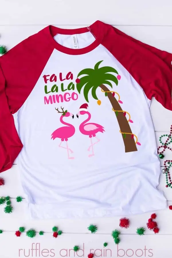 white shirt with red raglan sleeves on holiday background with flamingo Christmas svg featuring text which reads fa la la la mingo, two flamingoes in holiday accessories, and a palm tree in Christmas lights