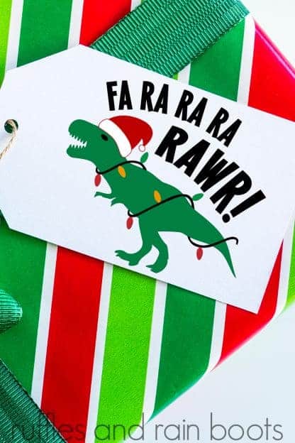 vertical image of t rex Christmas SVG on a white gift tag on a red and green striped package