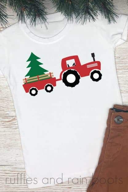 white t shirt with pine needles and brown pants on wood background with red green and black Christmas tractor svg