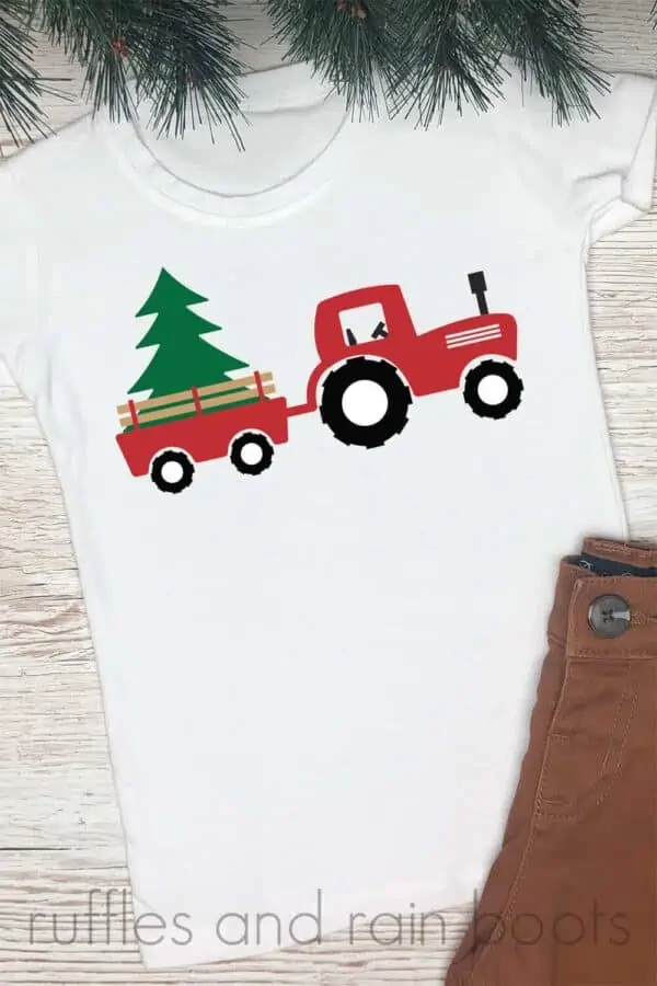 white t shirt with pine needles and brown pants on wood background with red green and black Christmas tractor svg