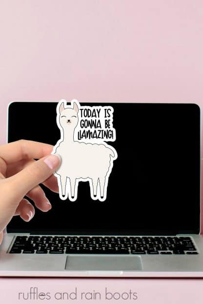 vertical image of today is gonna be llamazing sticker in hand in front of pink wall and black screen laptop