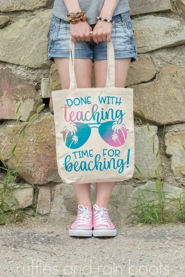 vertical image of woman in front of rock wall holding tote bag with done with teaching time for beaching in pink and blue sublimation print