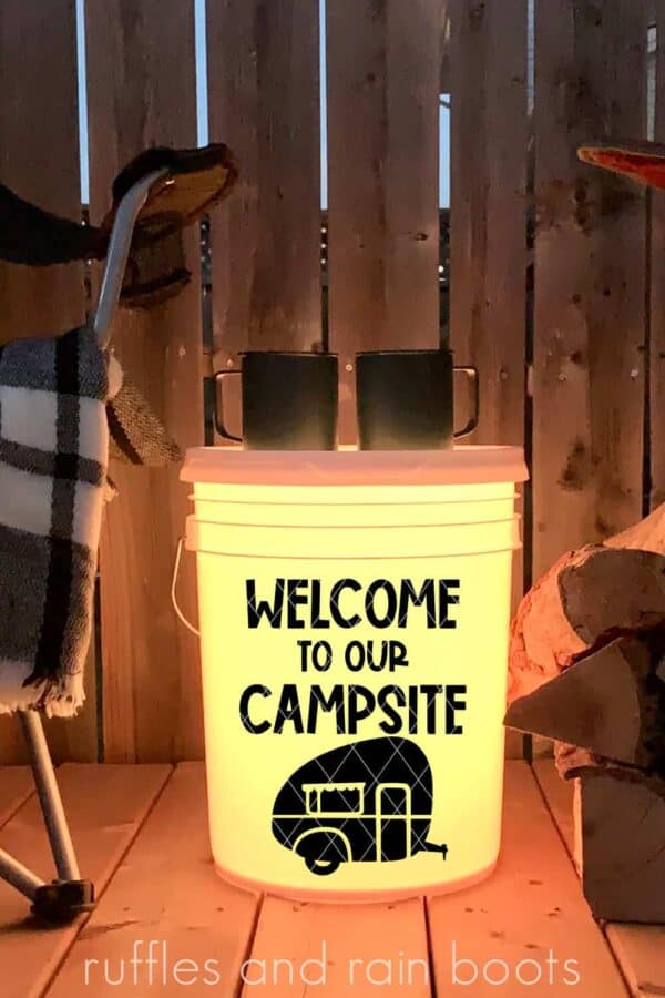 vertical image of yellow camp bucket with welcome to our campsite in black vinyl on wood porch