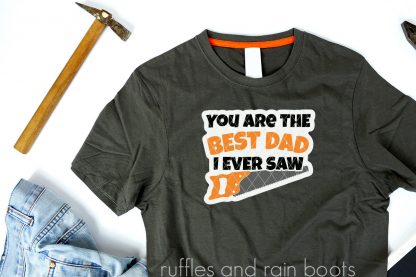 father's day SVG with saw in black orange and gray on gray t shirt on white background with hammer and jeans
