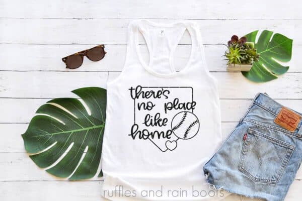 theres no place like home baseball svg in black on white tank top with tropical leaves and jean shorts on white wood background