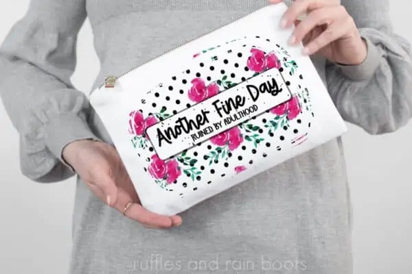 white woman in gray dress holding white makeup bag with another fine day ruined by adulthood sublimation in black polka dots and pink floral pattern