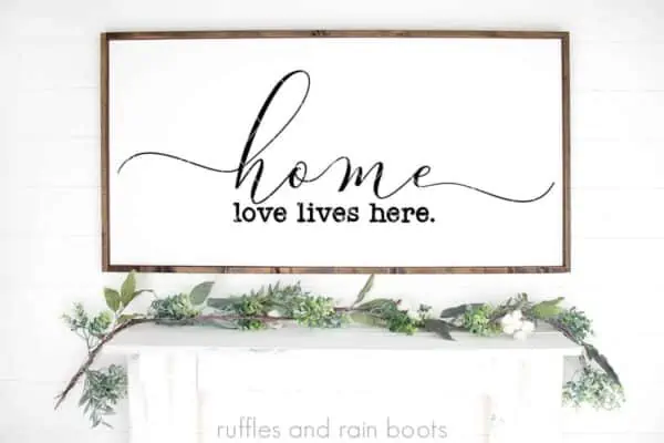 horizontal image of home svg love lives here cut file in black vinyl on wood sign on mantel and white background