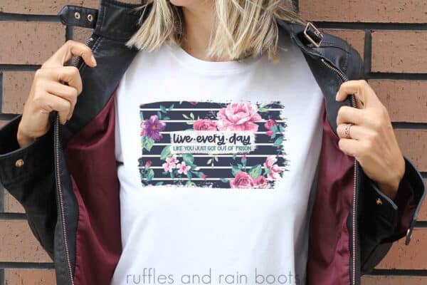 woman in white t shirt holding open black jacket with live every day like you just got out of prison sublimation in navy stripe and pink floral background