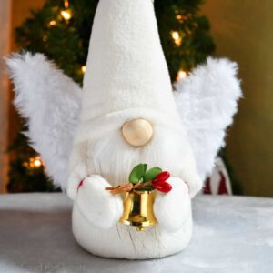 close up square image of an angel gnome holding a gold bell made with a free angel wing pattern from ruffles and rain boots