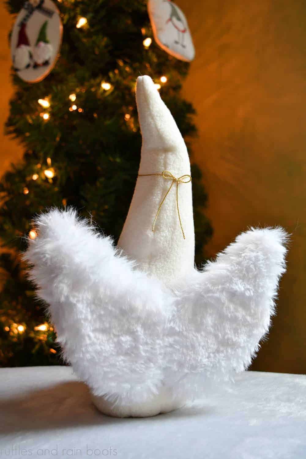 a back view of a gnome with angel wing pattern fluffy angel wings in front of Christmas tree