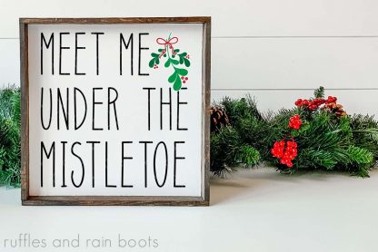 horizontal image of meet me under the mistletoe in black green and red vinyl on square wood tiered tray sign