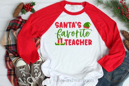 horizontal image of red raglan t shirt with Santa's favorite teacher SVG in red and green HTV with elf hat and shoes on Christmas background with pine and berries