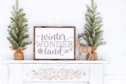 horizontal image of a Christmas mantle decorated with two flocked trees in burlap bags, a wood reindeer, and a Christmas sign with winter wonderland cut file and bonus snowflakes