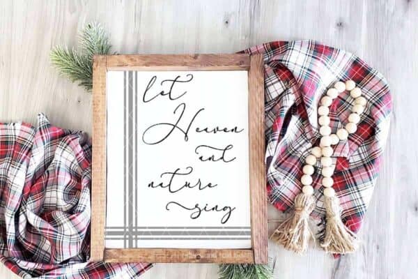 horizontal image of a wood frame with gray and black vinyl with let Heaven and nature sing svg on a wood background with Christmas scarf and farmhouse beads