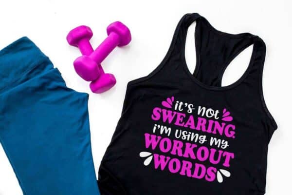 horizontal image close up of blue leggings pink dumb bells and black tank top with white and pink vinyl which reads its not swearing im using my workout words cut file