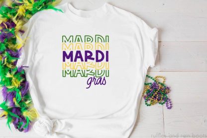 horizontal image of wood background with a white t shirt and green yellow and purple mardi gras svg in vinyl.