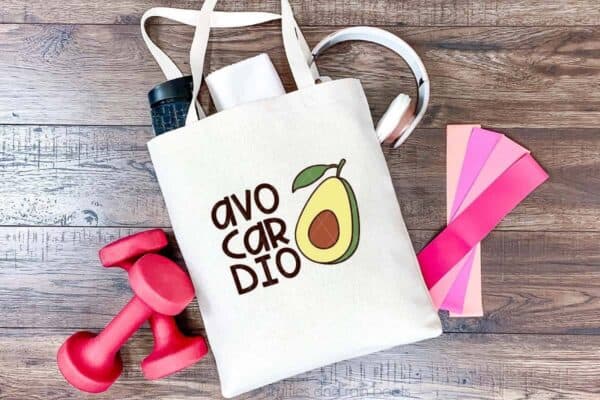 Avo cardio svg in vinyl on exercise tote bag on dark wood background with free weights and exercise straps.