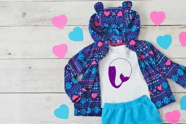 Horizontal image of a little girl outfit with dark purple mermaid tail monogram in purple vinyl on wood background with pink and teal hearts.