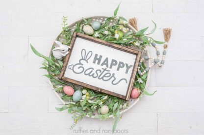 Horizontal image with a farmhouse basket full of greenery, Easter eggs, and prayer beads with a rectangle sign which reads Happy Easter with the cut file in gray vinyl for the Easter sign.