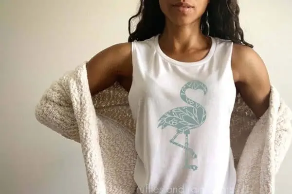 Woman standing in front of a beige wall wearing a cardigan and white tank top with a sage colored flamingo mandala made with the free cut file.