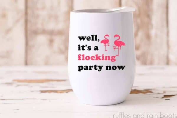 Horizontal image of white stemless wine tumbler with black and pink vinyl which reads well, it's a flocking party now with two flamingos holding cocktails.