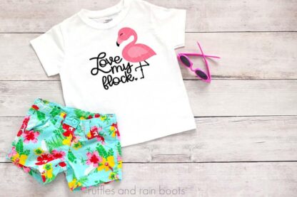 Floral shorts, sunglasses, and white toddler t shirt with love my flock and kawaii flamingo SVG in pink and black vinyl made on Cricut cutting machine.