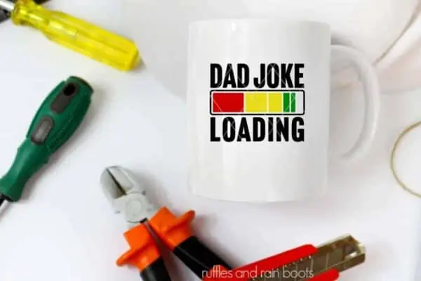 Horizontal image of white mug with dad joke loading svg in color on white background with tools.