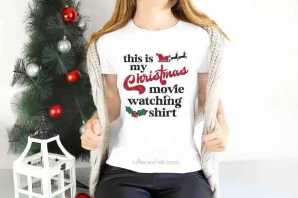 Horizontal image of small holiday tree and woman in white t-shirt with this is my Christmas movie watching shirt SVG in red, black, and green HTV.