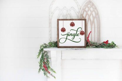 Horizontal image of a Christmas sign with Jingle SVG with sleigh bells on a mantle with greenery and frames.