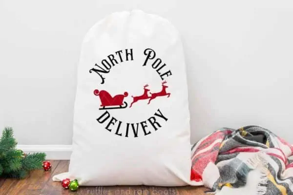 Horizontal image of a white Santa sack with the stamp style North Pole Delivery SVG in black and red vinyl with reindeer and sleigh.