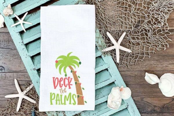 Horizontal image of a white kitchen waffle towel on light blue shutter on beach background with deck the palms cut file in vinyl.