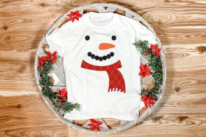 Horizontal image of a snowman face in heat transfer vinyl on a white toddler t-shirt placed in a Christmas basket on wood background.