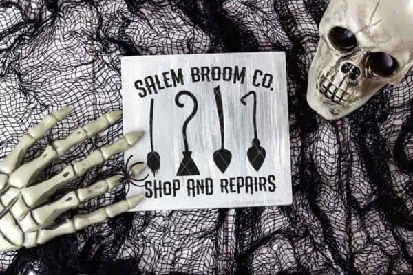 Horizontal image of a Halloween background with mesh, skull, and hand and a white wood Salem Broom Co SVG in black vinyl.
