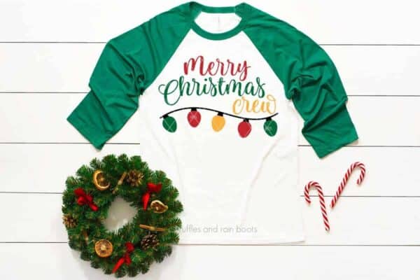 Horizontal image of a green raglan shirt with a Merry Christmas Crew SVG in red, green, and yellow with festive background.