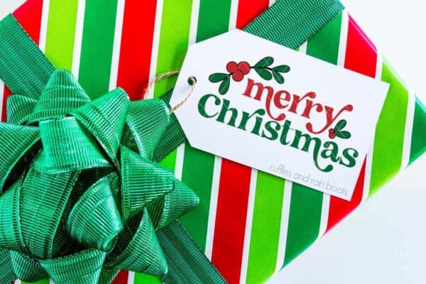 Horizontal image of a red, white, and green gift with big, green bow and white gift tag with merry Christmas and holly.
