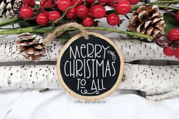 Horizontal close up image of a wood ornament painted black with white vinyl which reads Merry Christmas to All with holly and berries.
