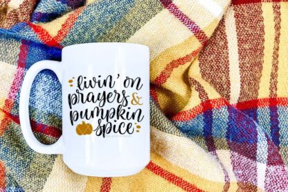 Horizontal image of white mug with livin' on prayers and pumpkin spice svg in black and mustard vinyl.