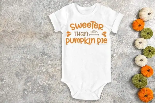 Horizontal image of white baby body suit on concrete which reads sweeter than pumpkin pie in vinyl.