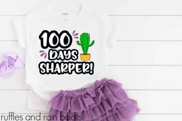 Purple ruffle skirt and white t-shirt which reads 100 days sharper with a cactus SVG on white wood background.