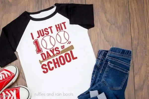 Horizontal image of a raglan t-shirt on wood background with I just hit 100 days of school with baseballs and bat.