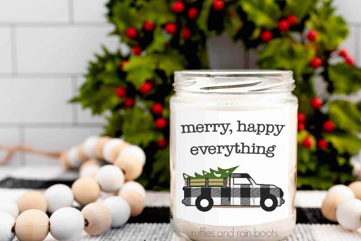 Horizontal image of white candle with label which reads merry, happy everything with a white plaid Christmas truck.