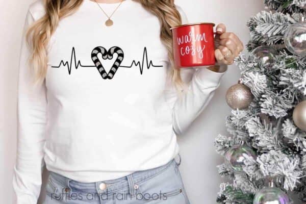 Horizontal image of woman in white long sleeve t shirt with Christmas heartbeat candy cane design in black and silver glitter vinyl.