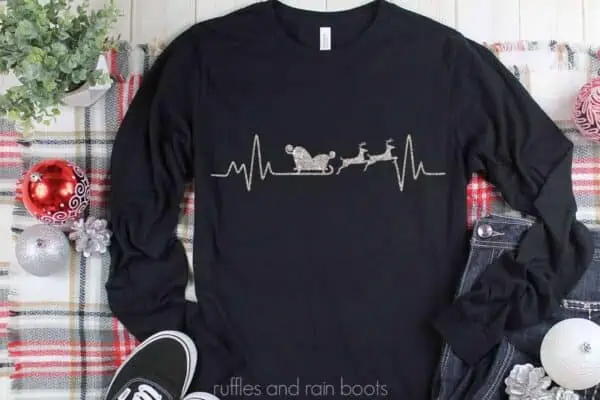 Horizontal image close up of black long sleeve t shirt with silver glitter vinyl of Christmas sleigh heartbeat design.