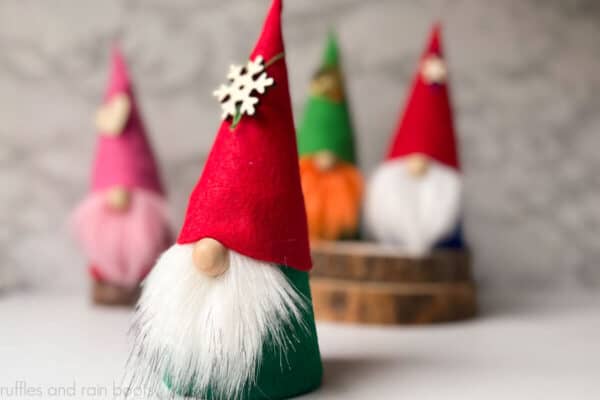 Horizontal image close up of a Christmas gnome with red hat, green body, and white beard in front of blurred gnomes in background.